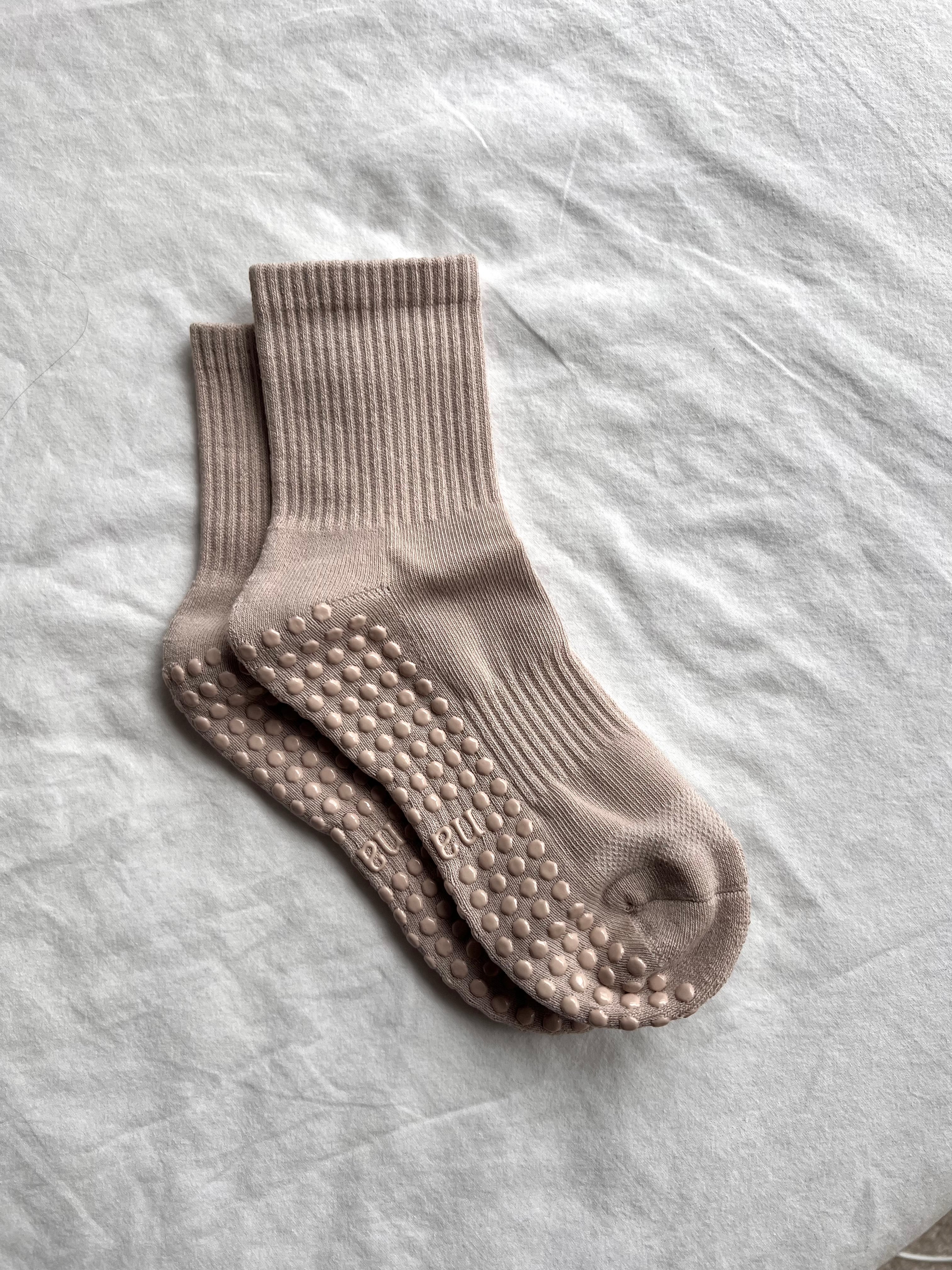 Pair of beige socks with textured sole on a light gray fabric background